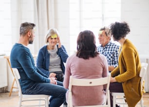 Men and women sitting in a circle during group therapy, adhesive notes with negative emotions on forehead.