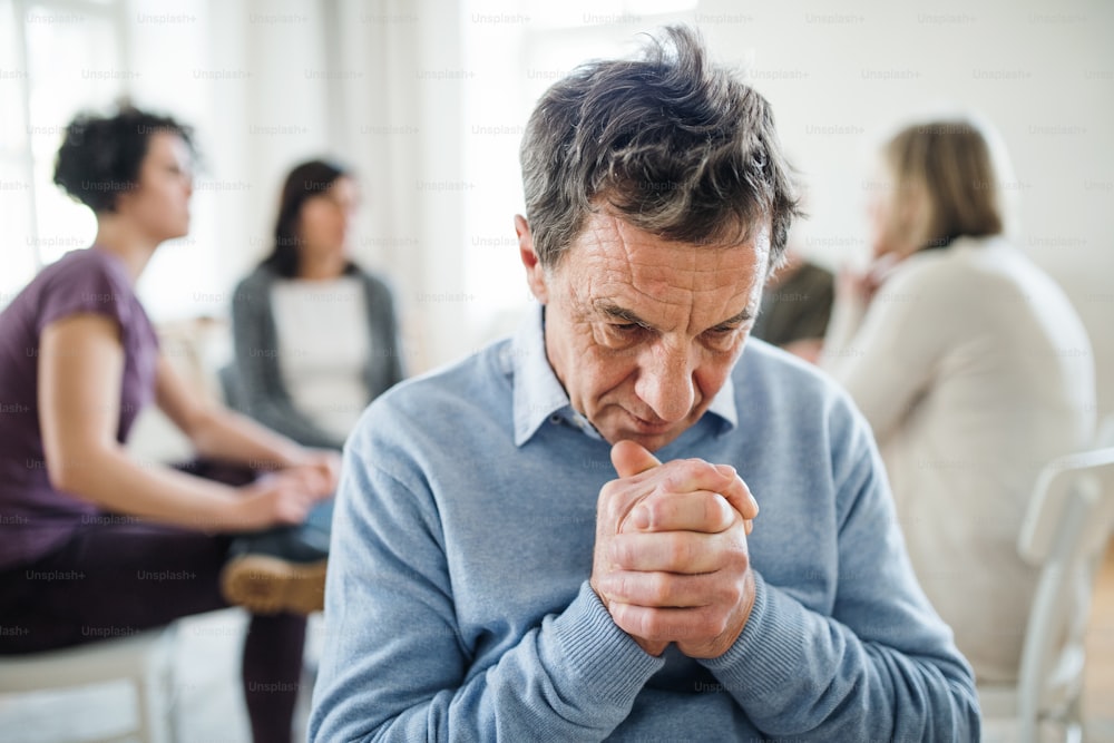 A portrait of senior depressed man during group therapy, looking down.