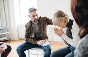 A senior depressed woman crying during group therapy, other people comforting her.