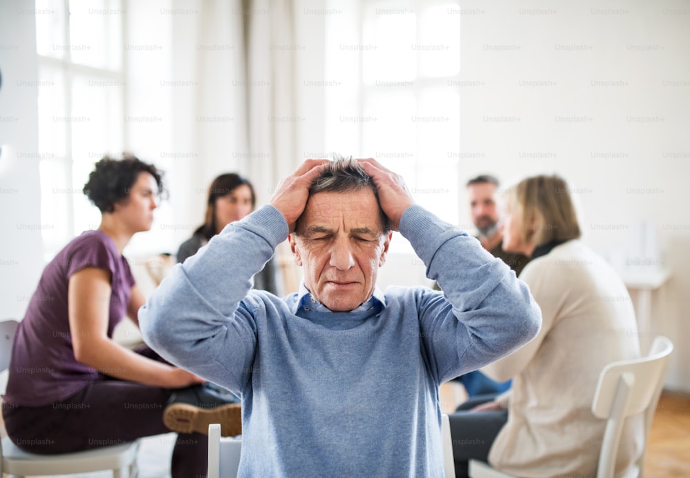 A waist-up portrait of senior depressed man during group therapy.