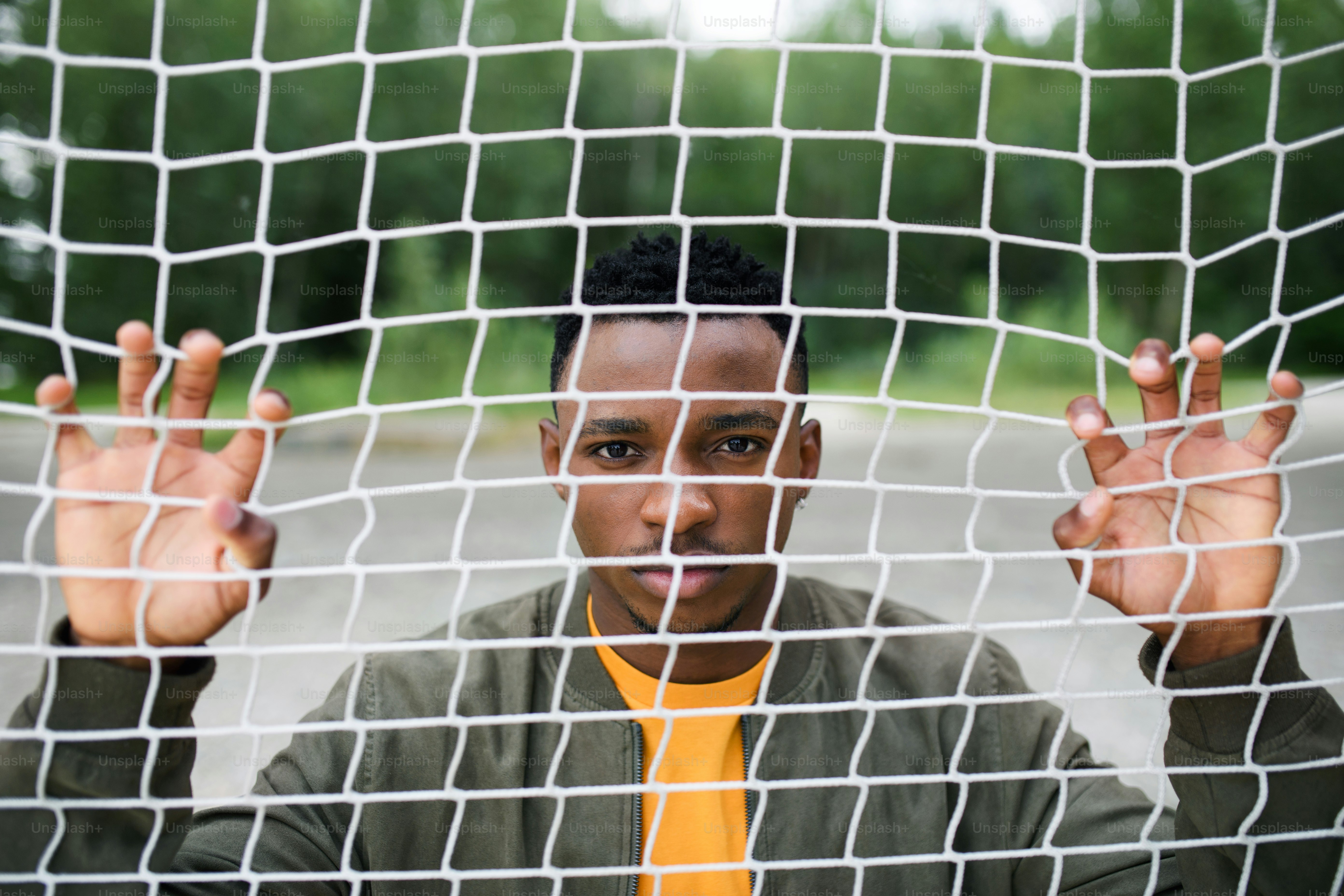 Frustrated young black man behind net outdoors in city, protest and discrimination concept.