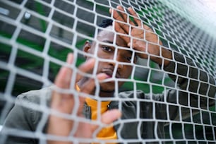 Frustrated young black man behind net outdoors in city, protest and discrimination concept.