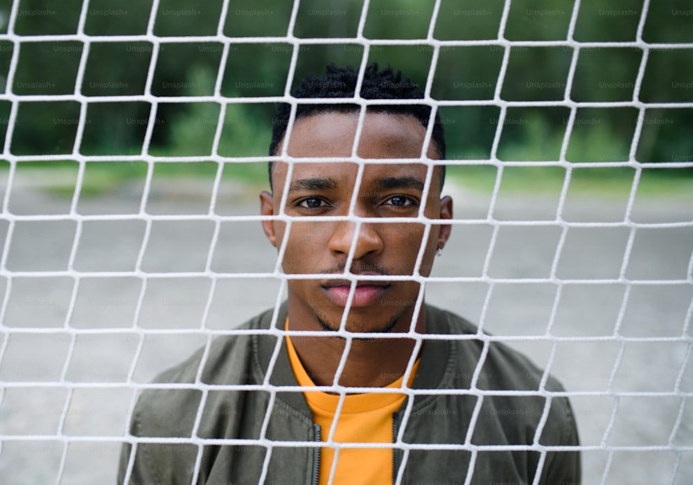 Frustrated young black man behind net outdoors in city.