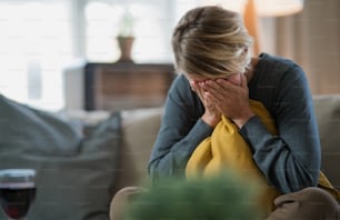 Sad and stressed woman indoors on sofa at home crying, mental health and coronavirus concept.