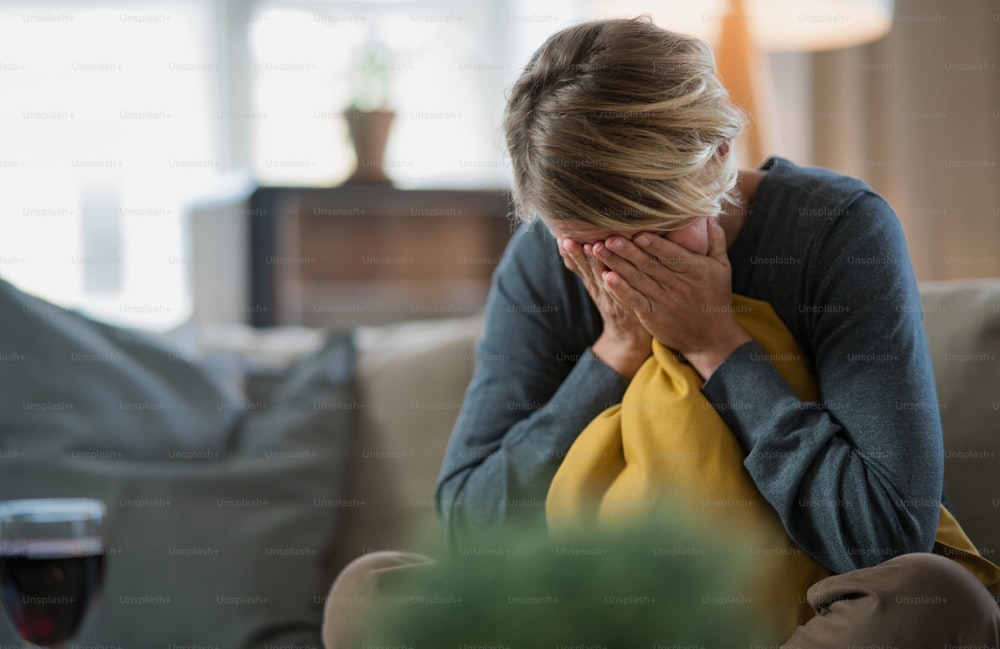 Mujer triste y estresada en el interior en el sofá de casa llorando, salud mental y concepto de coronavirus.