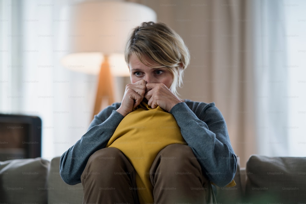 Worried woman with tablet indoors on sofa at home feeling stressed, mental health concept.