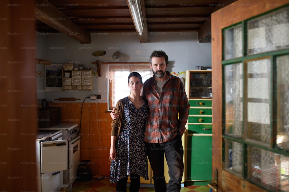 Retrato de triste casal pobre maduro olhando para a câmera dentro de casa em casa, conceito de pobreza.