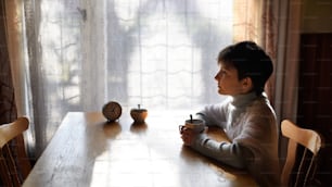 Vista lateral de la pobre niña triste con té sentada a la mesa en el interior de casa, concepto de pobreza.