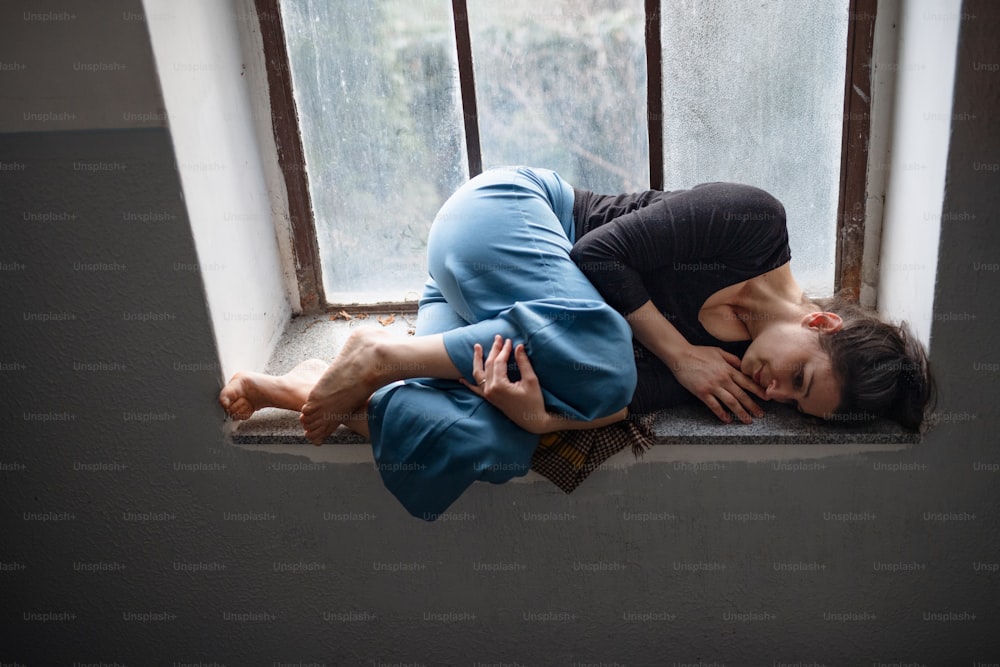 Portrait d’une femme seule allongée sur un vieux rebord de fenêtre sale, concept de solitude, de santé mentale et de dépression.