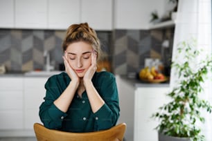 Un ritratto di una giovane studentessa stanca seduta e rilassata con gli occhi chiusi al chiuso in cucina.