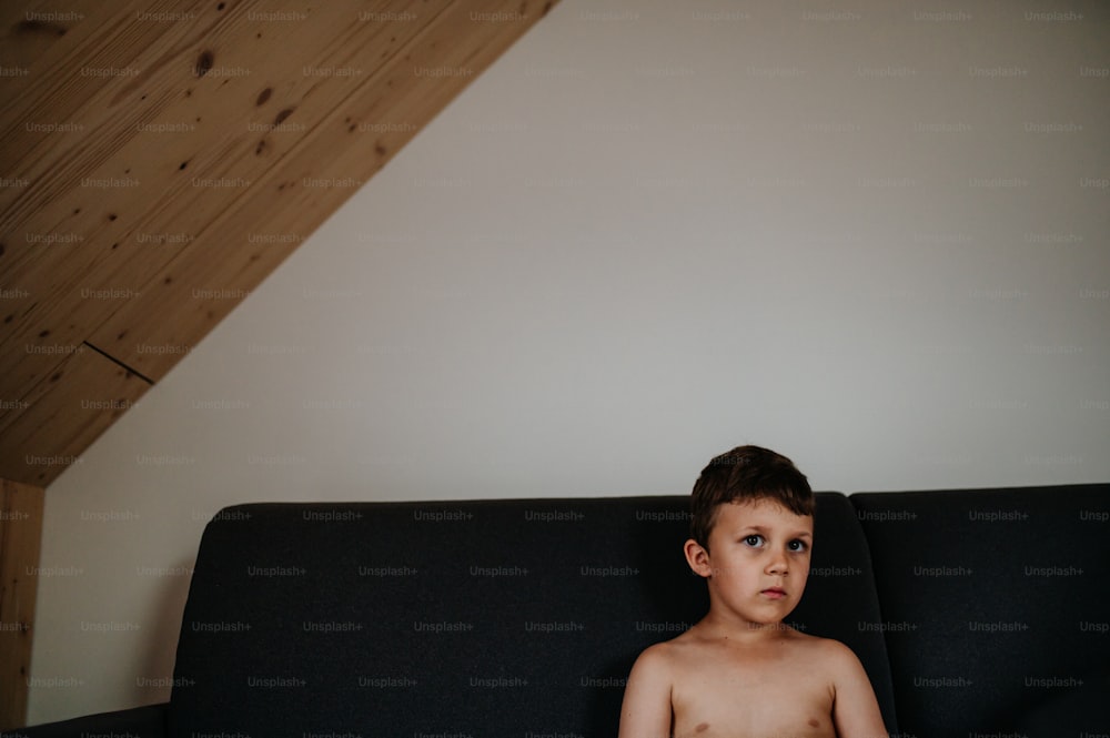 A portrait of sad little boy sitting on sofa alone.