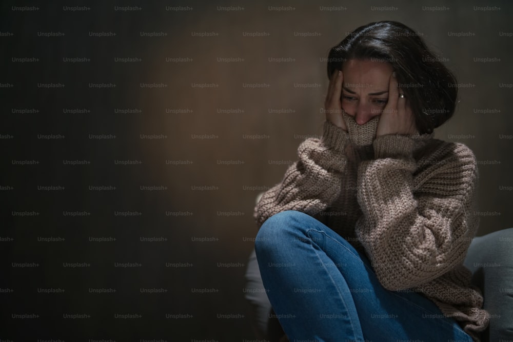 Eine depressive Frau im mittleren Erwachsenenalter, die im Dunkeln auf dem Boden sitzt und weint.