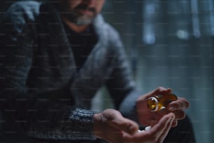 A mature man taking drug pill on dark background, mental health concept.