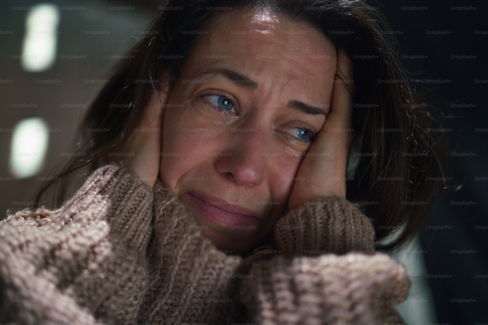 Um close-up de uma mulher solitária deprimida do meio do adulto chorando no escuro.