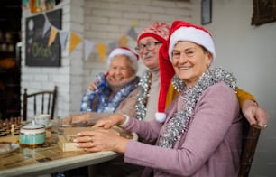 Amigos idosos felizes sentados dentro de casa em um centro comunitário e celebrando o Natal.