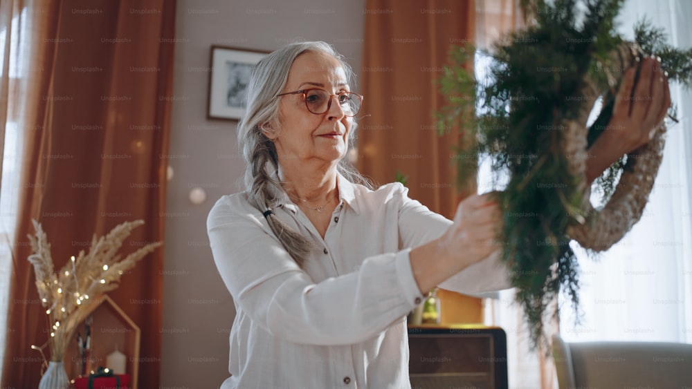 Senior woman a making Christmas wreath from natural materials indoors at home