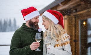 Coppia matura felice che beve vino sulla terrazza all'aperto nella natura invernale, vacanza nel periodo natalizio.
