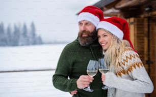 Happy mature couple drinking wine on terrace outdoors in winter nature, holiday at Christmas time.
