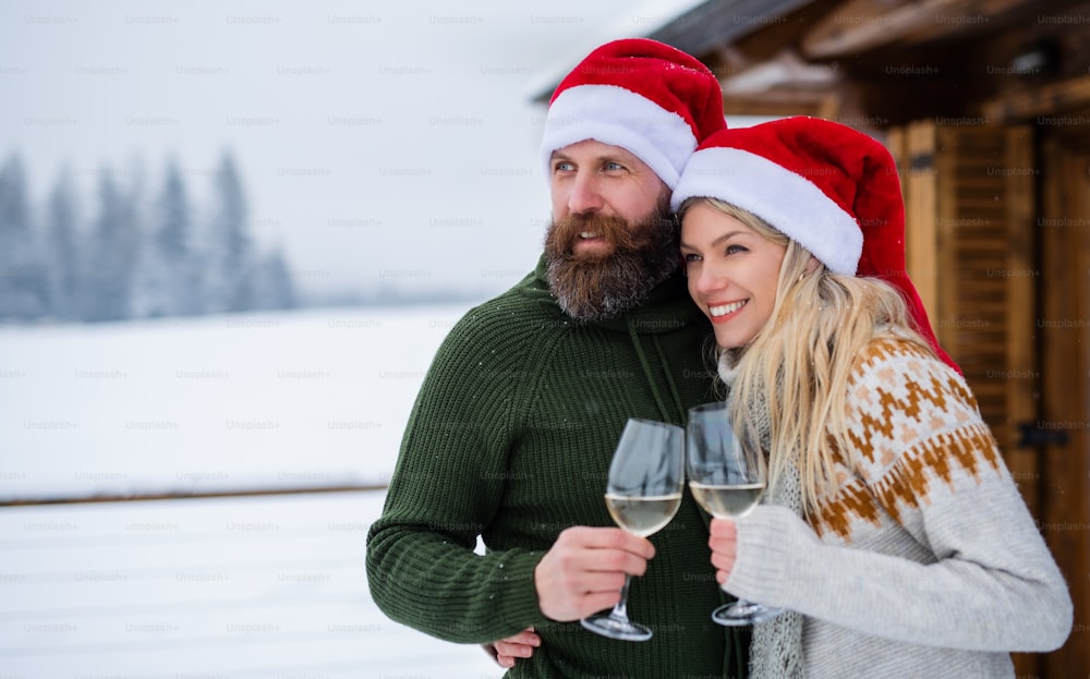 冬の自然の屋外テラスでワインを飲む幸せな成熟した夫婦、クリスマスの休日。