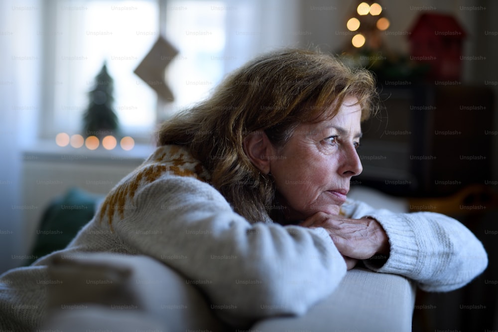 Porträt einer einsamen älteren Frau, die zu Weihnachten drinnen auf dem Sofa sitzt, Einsamkeitskonzept.