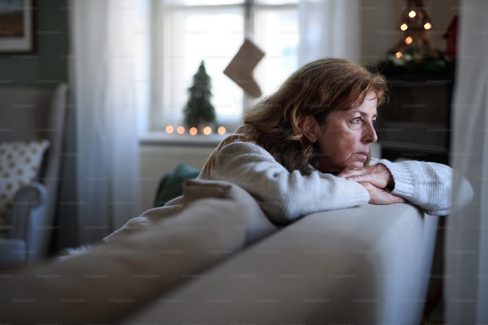 Porträt einer einsamen älteren Frau, die zu Weihnachten drinnen auf dem Sofa sitzt, Einsamkeitskonzept.