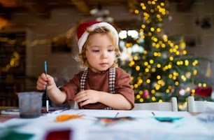 크리스마스에 집에서 실내에 있는 행복한 어린 소녀의 초상화, 그림을 그린다.