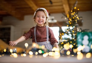 Portrait d’une petite fille heureuse à l’intérieur à la maison à Noël, riant.