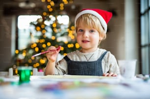 Portrait of happy small boy indoors at home at Christmas, painting pictures.