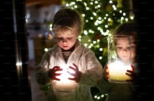 クリスマスに自宅でろうそくを持つ幸せな小さな女の子と男の子のポートレート。