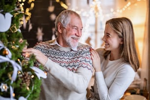 Happy young woman with senior grandfather indoors at home at Christmas, decorating tree.