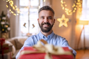Portrait of mature man indoors at home at Christmas, holding present.