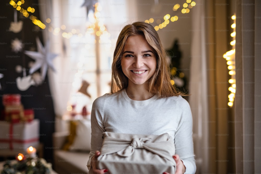 Retrato de una joven feliz en el interior de su casa en Navidad, sosteniendo el regalo.