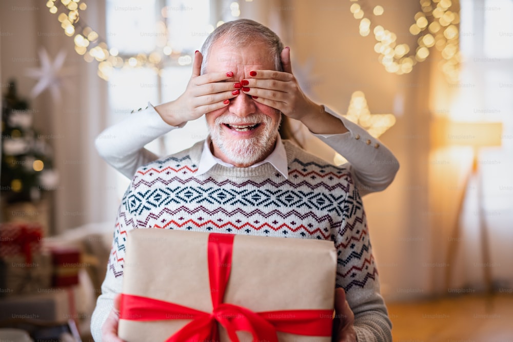 Unrecognizable young woman giving present to senior grandfather indoors at home at Christmas, midsection.