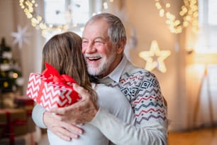 Portrait of young woman giving present to happy grandfather indoors at home at Christmas.