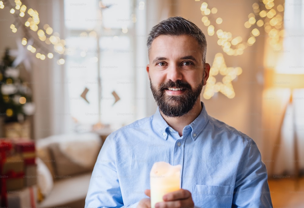 Portrait of mature man indoors at home at Christmas, holding candle.