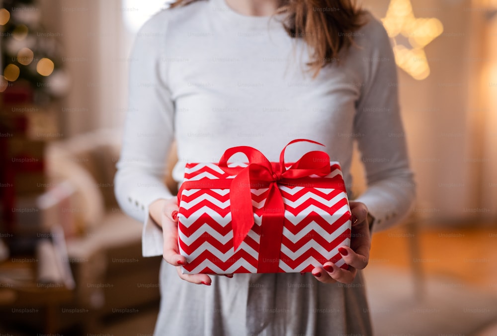 Midsection of unrecognizable young woman indoors at home at Christmas, holding present.