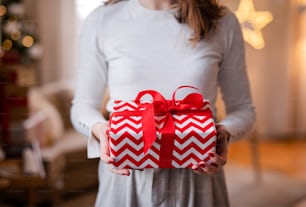Section médiane d’une jeune femme méconnaissable à l’intérieur à la maison à Noël, tenant un cadeau.