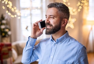 Retrato de hombre maduro en el interior de su casa en Navidad, usando un teléfono inteligente.