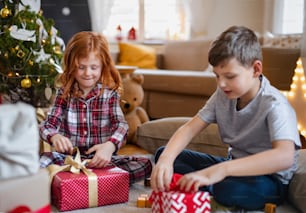 Small girl and boy in pajamas indoors at home at Christmas, opening presents in the morning.