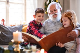 Portrait of small children with senior grandfather indoors at home at Christmas, looking at photographs.