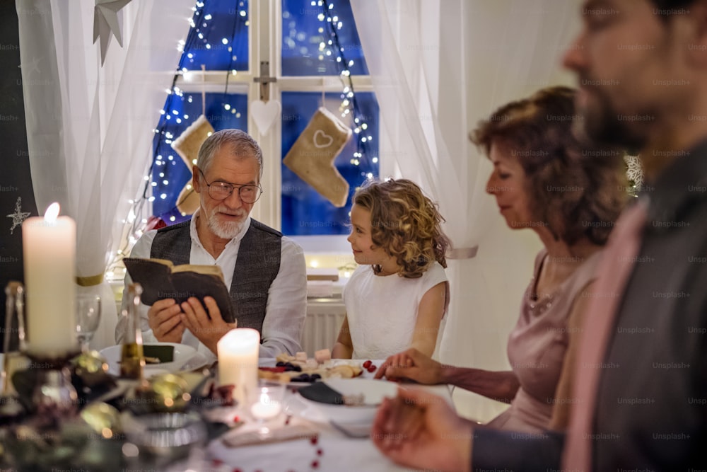 Happy senior man with extended family indoors celebrating Christmas, reading Bible.