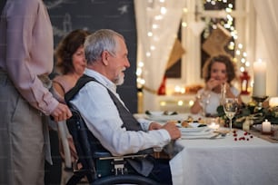 Feliz hombre mayor en silla de ruedas con la familia en el interior celebrando la Navidad juntos.