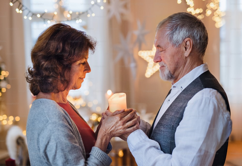 Side view portrait of happy senior couple indoors celebrating Christmas, holding candle.