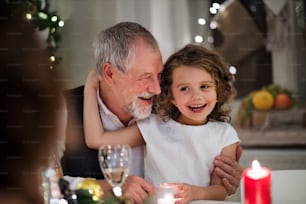 Nonno anziano felice con la piccola nipote in casa a Natale, seduto a tavola.