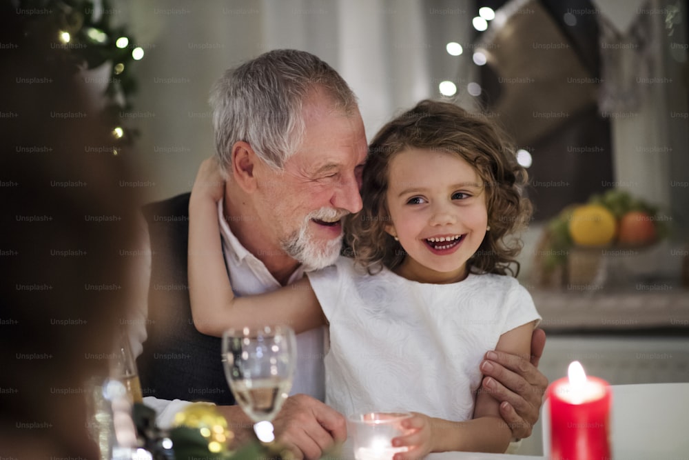 Grand-père aîné heureux avec une petite petite-fille à l’intérieur à Noël, assis à table.