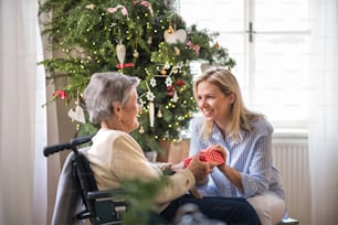 A health visitor and a senior woman in wheelchair with a present at home at Christmas time.