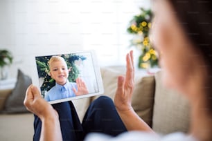 Una nonna irriconoscibile con tablet che fa videochiamata con il nipotino nel periodo natalizio, salutando.