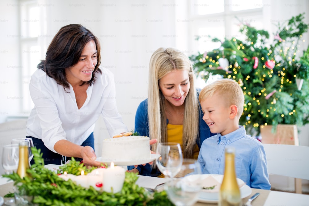 A small boy with motherlooking at grandmother putting a cake on table at home at Christmas time.