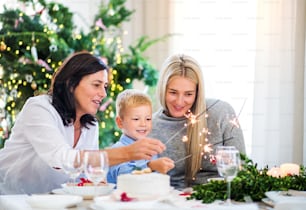 Un niño pequeño con madre y abuela sentadas en una mesa en Navidad, sosteniendo destellos.