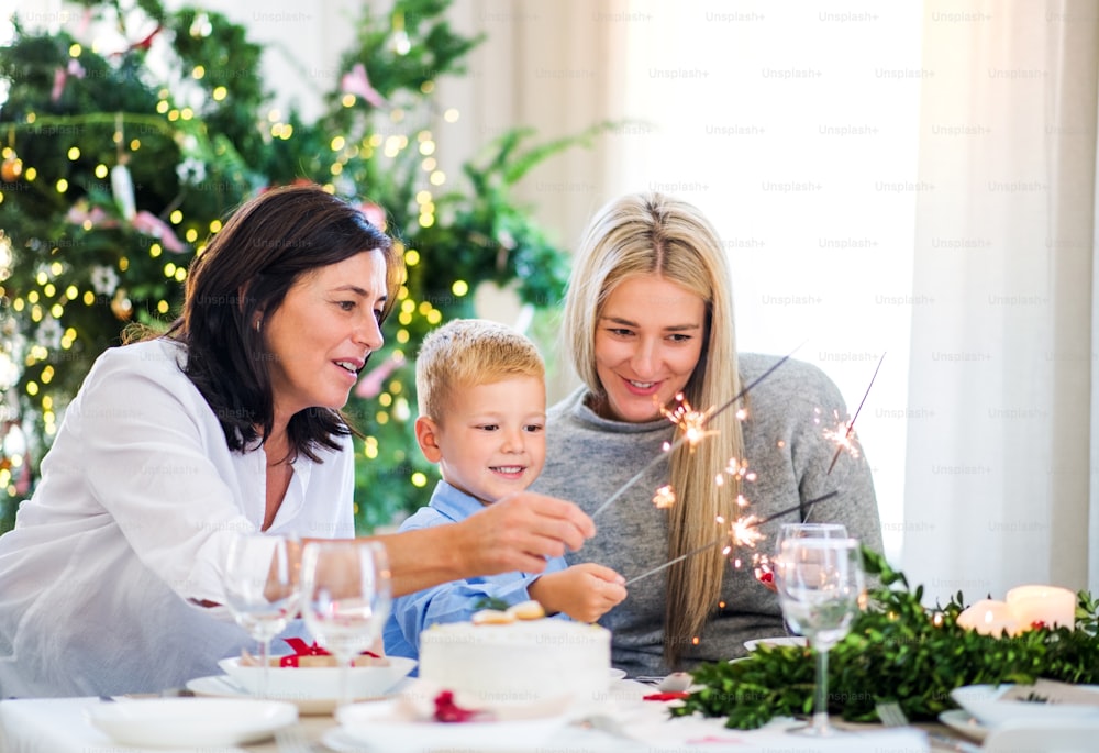 Un petit garçon avec mère et grand-mère assis à une table au moment de Noël, tenant des étincelles.
